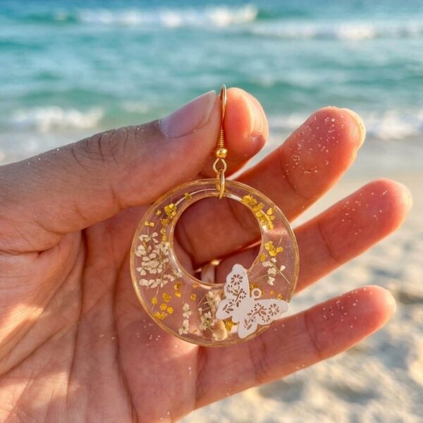 Détail breloque résine avec papillons blancs, fleurs naturelles et paillettes or.