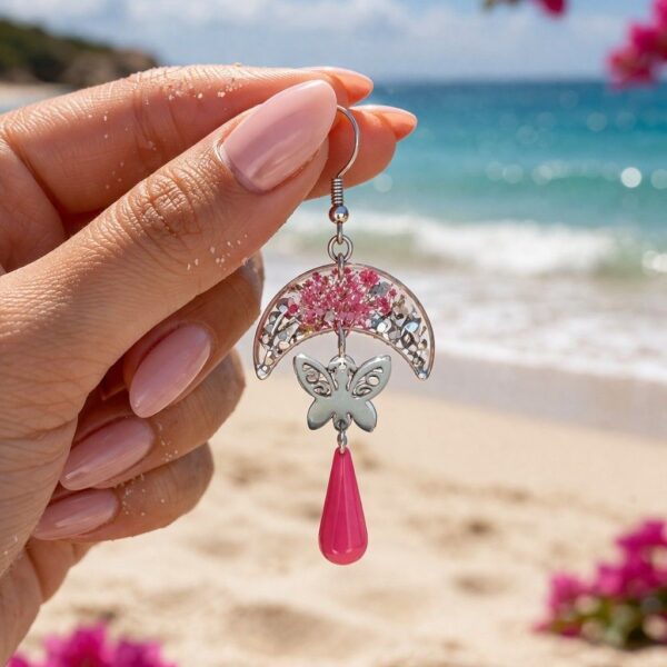 Gros plan des boucles Pauline portées, montrant le mouvement des papillons et la transparence lumineuse de la résine fuchsia."