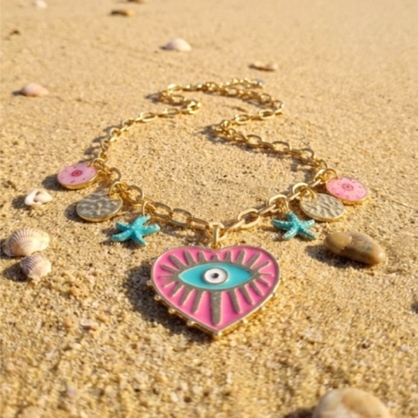 Succombez au charme méditerranéen avec le collier Milos. Une chaîne dorée ornée d'un cœur protecteur et de breloques marines pour un style bohème irrésistible.