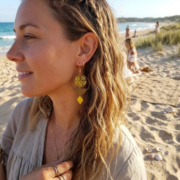 "Mise en situation des boucles d'oreilles Yara portées, révélant leur superbe asymétrie et l'éclat lumineux des fleurs séchées jaunes sur l'oreille."