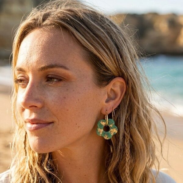 Plan rapproché sur le profil d'une femme portant la créole Flavy, côté résine verte émeraude et paillettes dorées visible. Le bijou capte la lumière.