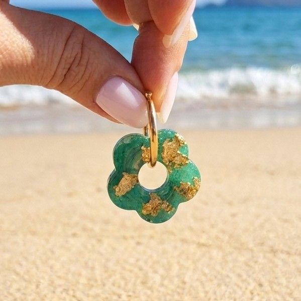 Gros plan d'une paire de boucles d'oreilles créoles dorées avec des pendentifs fleurs en résine verte et pétales dorées