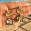 Boucles d'oreilles fleurs Clémence en papier calligraphié zébré tenues dans une main sur la plage
