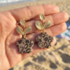 Boucles d'oreilles fleurs Clémence en papier calligraphié léopard tenues dans une main sur la plage
