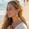 Boucles d'oreilles fleur arbre doré Clémence portée à l'oreille par une femme style bohème sur la plage