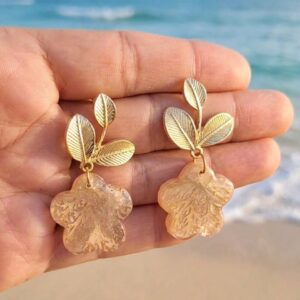 Boucles d'oreilles fleurs Clémence en papier calligraphié tenues dans une main sur la plage