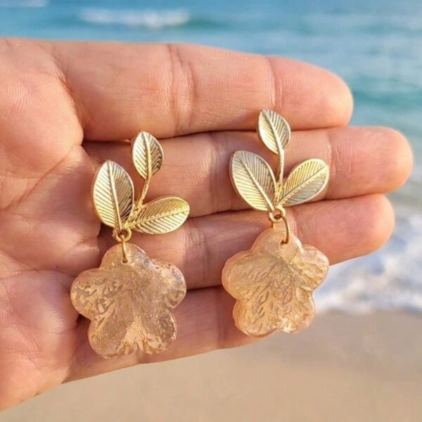 Boucles d'oreilles fleurs Clémence en papier calligraphié tenues dans une main sur la plage