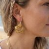 Créoles fleurs Capucine côté nacré doré portée par une femme sur une plage