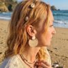 Boucle d'oreille demi-lune Naya motif arbre doré portée par une femme blonde sur la plage - L.F.K Créations